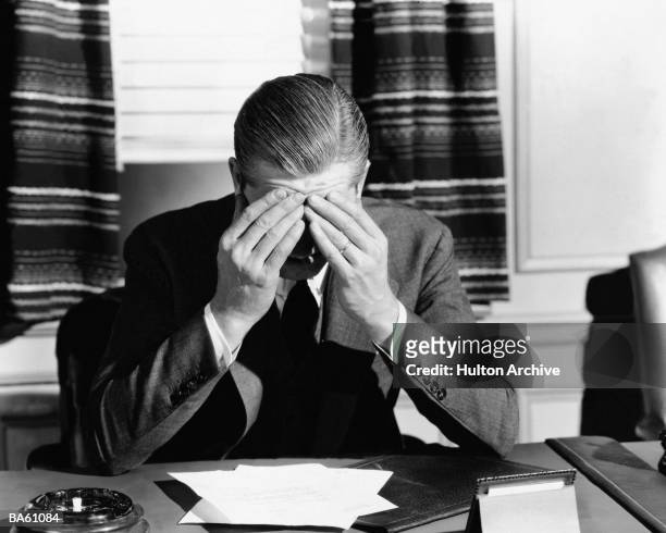 Businessman sits at his office desk, holding his