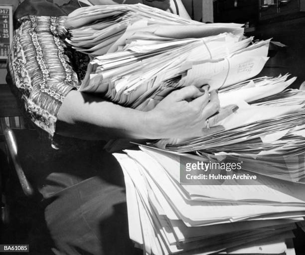 View of a woman's arms struggling to hold stacks of business papers, 1960s