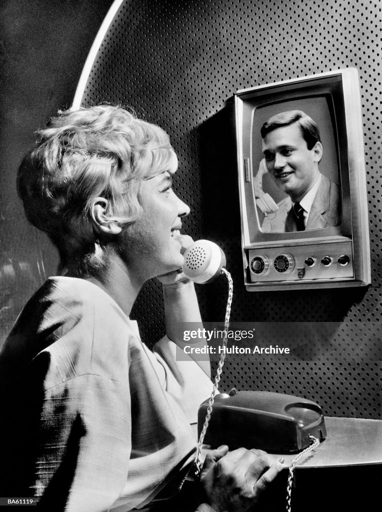 Woman using telephone, talking to man on screen (B&W)