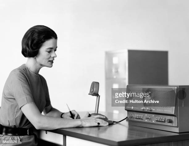 Woman sits at a desk, speaking into an intercom