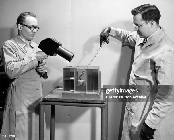 Two scientists wearing white lab coats heat a petri dish while performing an experiment, 1940s