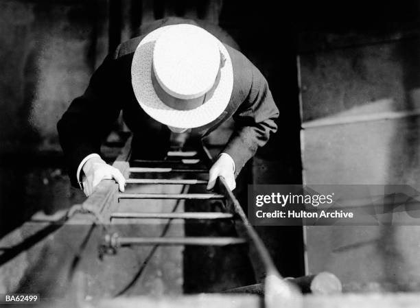 Man wearing a boater climbing a ladder. July 190