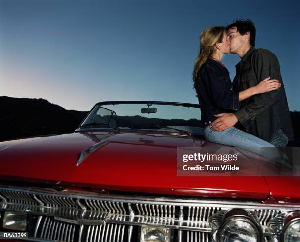 young couple kissing on bonnet of convertible car - car hood stock pictures, royalty-free photos & images