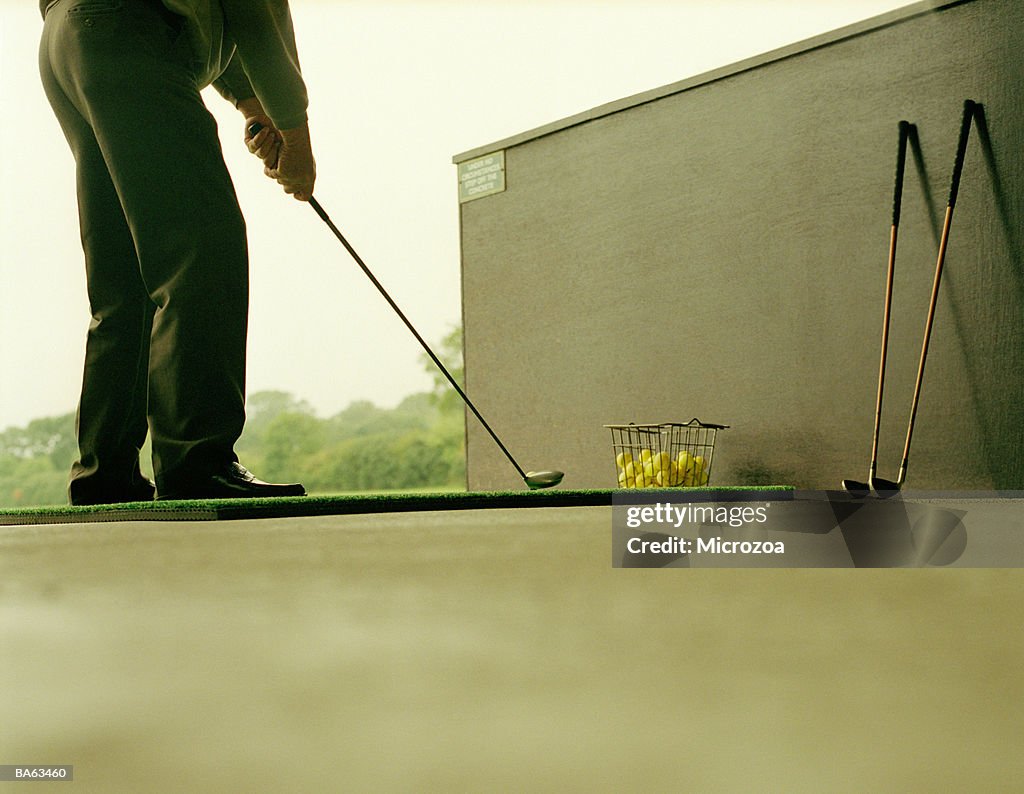 Male golfer lining up stroke on practice range, low section
