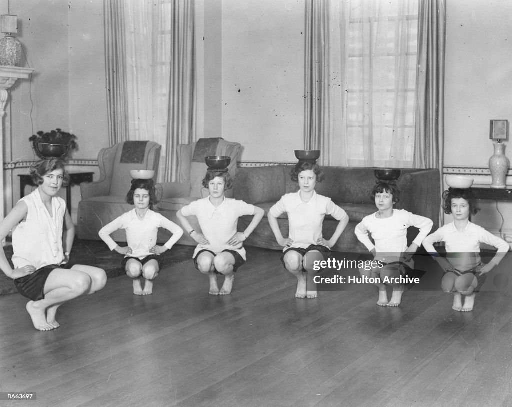 Line of girls (7-12) exercising with bowls on heads (B&W)