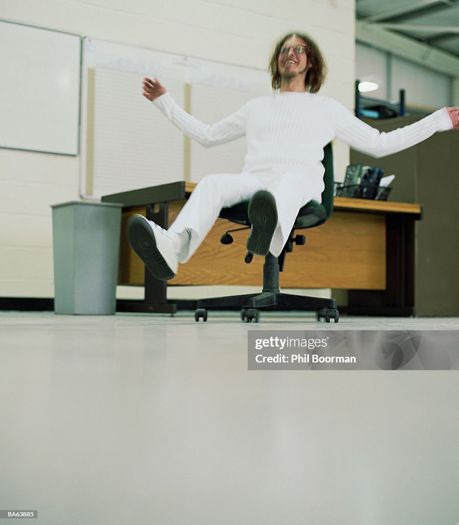 Man sliding across floor on office chair (blurred motion)