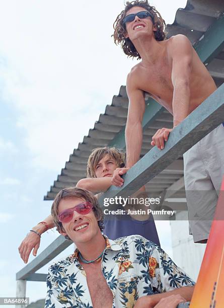 three young men leaning on veranda of beach hut, low angle view - justin stock pictures, royalty-free photos & images