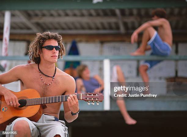 young man playing acoustic guitar in front of beach hut - justin stock pictures, royalty-free photos & images