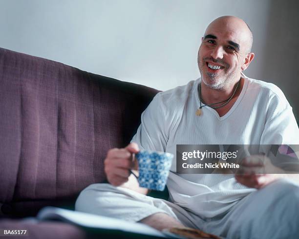 man on sofa with mug of tea and piece of toast, smiling, portrait - white tea stock pictures, royalty-free photos & images