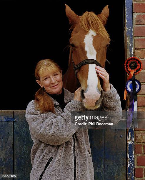 mature woman stroking horses' nose over stable door, portrait - phil stock pictures, royalty-free photos & images