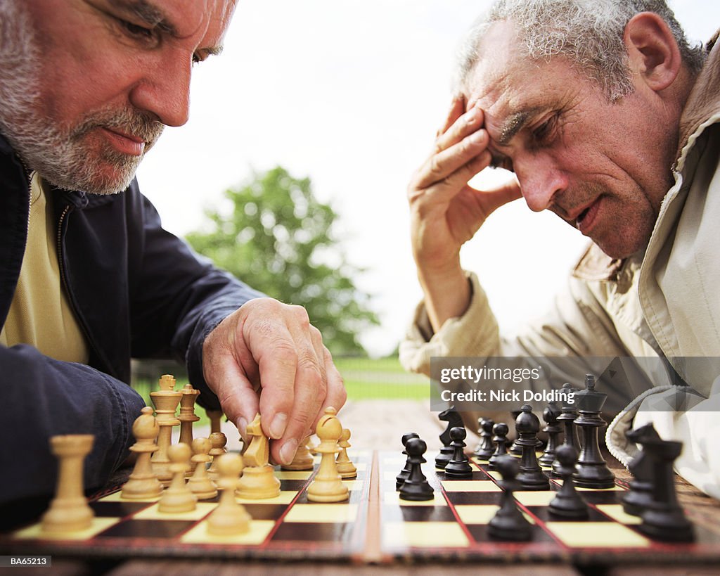 Two mature men playing chess on picnic table in park, close-up