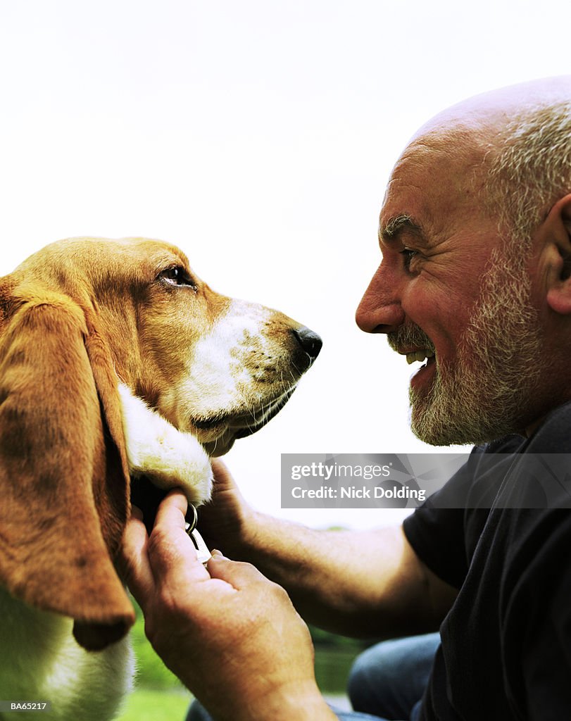 Mature man facing basset hound, outdoors, close-up