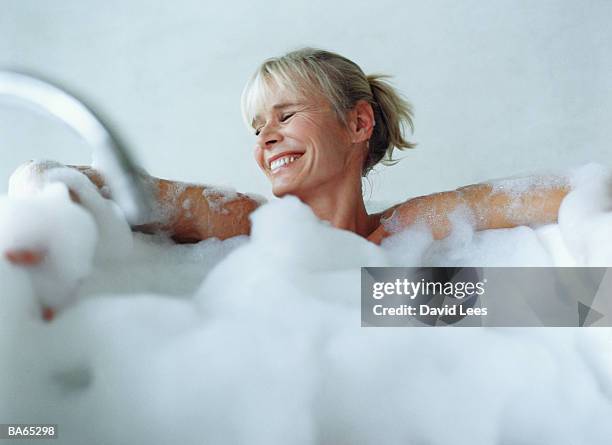 mature woman relaxing in bubble bath, smiling - domestic bathroom stock pictures, royalty-free photos & images