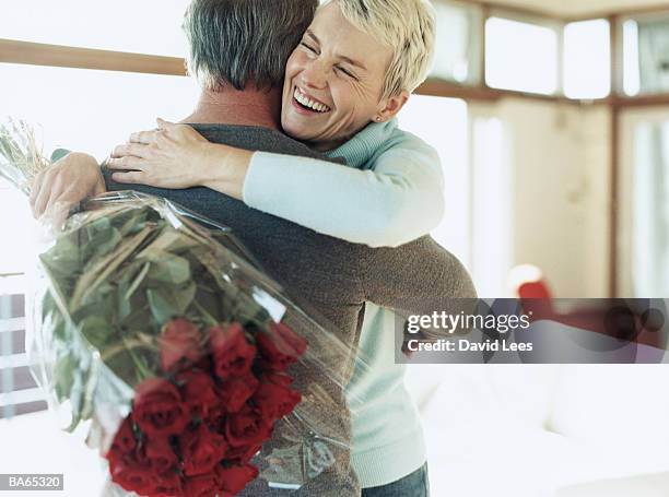 mature couple embracing, woman holding bunch of red roses - sorry stock pictures, royalty-free photos & images