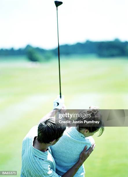 man helping woman with golf swing, rear view - justin stock pictures, royalty-free photos & images