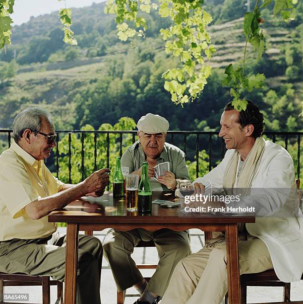 mature man and two elderly men playing cards outdoors - senior men playing cards stock pictures, royalty-free photos & images