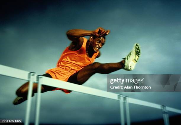 man clearing hurdle, against grey sky (digital enhancement) - hurdling track event fotografías e imágenes de stock