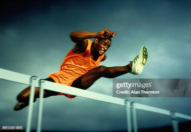 man clearing hurdle, against grey sky (digital enhancement) - hordelopen atletiekonderdeel stockfoto's en -beelden