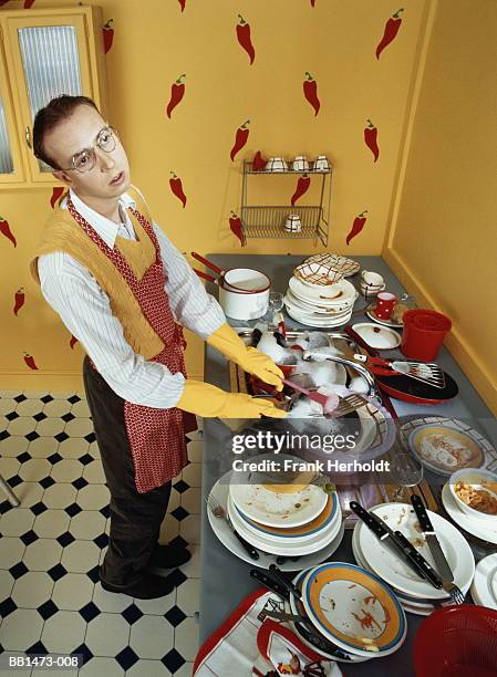 man wearing apron and rubber gloves washing up dirty dishes in kitchen - vaisselle sale photos et images de collection