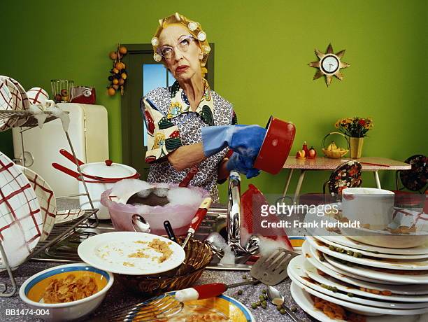 mature woman wearing hair rollers, washing up dirty dishes - schmutzig stock-fotos und bilder