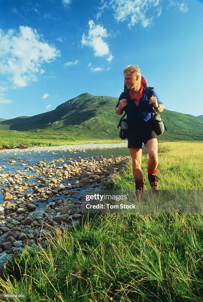 Male hiker walking beside stream, Glenn Orrin, Scotland