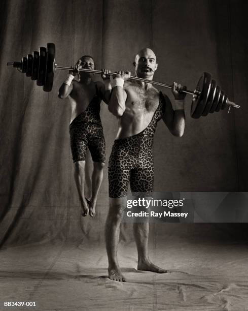 circus dwarf hanging from barbell lifted by strongman (tinted b&w) - little people stock pictures, royalty-free photos & images