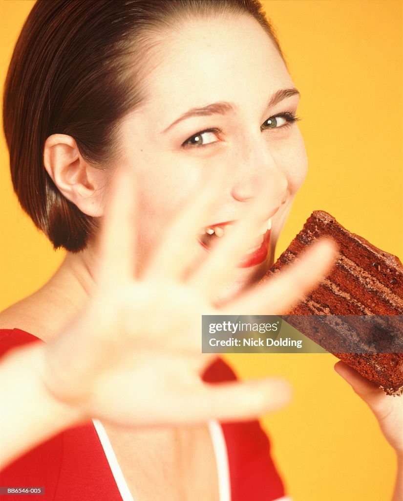 Young woman eating chocolate cake, holding hand in front of face