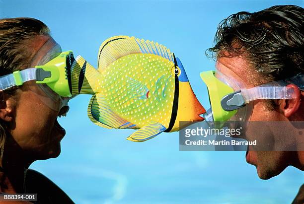 couple in diving masks, balancing toy fish between them - crazy holiday models stock pictures, royalty-free photos & images