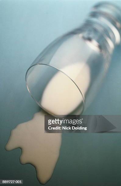 drinking glass lying on its side, milk spilt on surface (b&w) - spilt milk foto e immagini stock