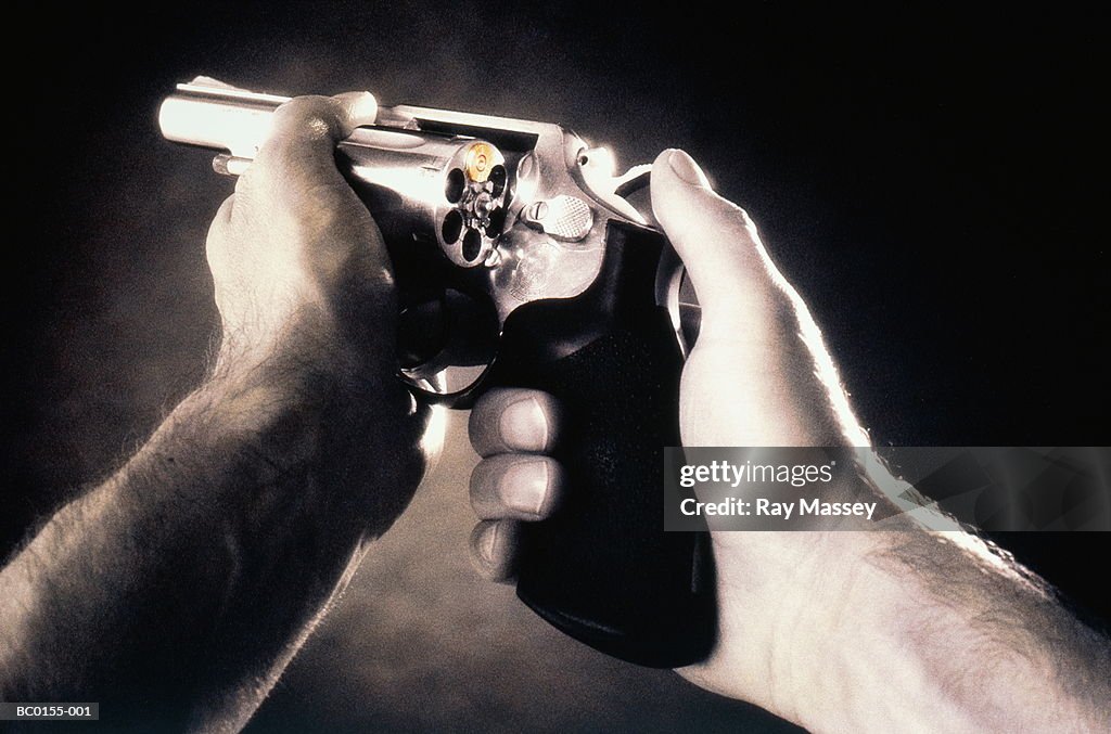 Mans' hands holding handgun loaded with single bullet (tinted B&W)