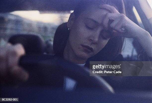 young woman at wheel of car, eyes closed, with hand on head (grainy) - files stockfoto's en -beelden