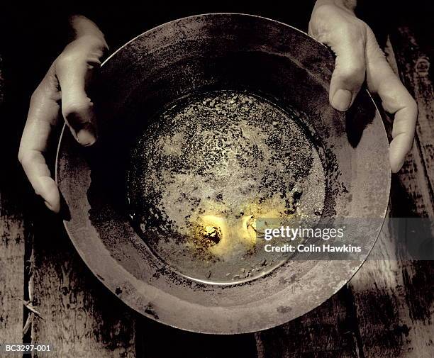 man holding pan containing nuggets of gold, close-up (tinted b&w) - gold waschen stock-fotos und bilder