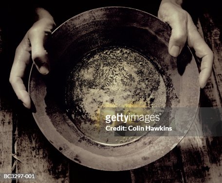 Man holding pan containing nuggets of gold, close-up (tinted B&W)