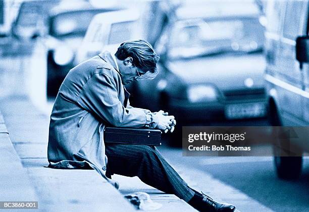 despondent looking businessman, sitting on edge of curb (toned b&w) - crisis de los cuarenta fotografías e imágenes de stock