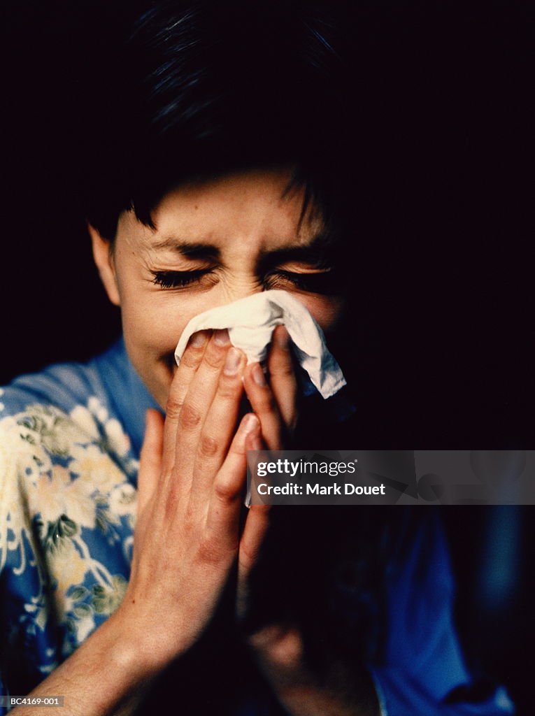 Young woman using hankerchief, eyes tightly shut, close-up