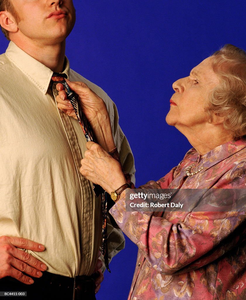 Elderly woman tying young man's tie, close-up