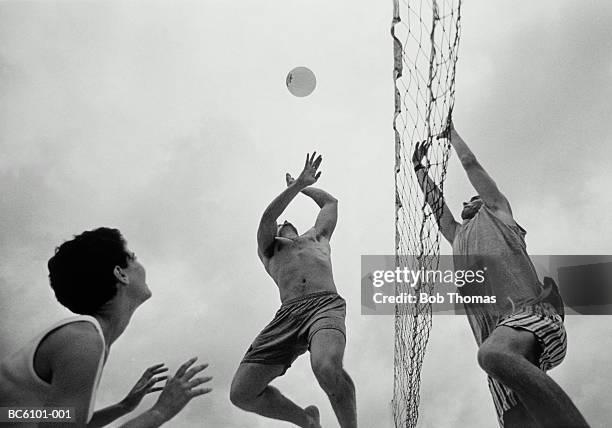 two young men and one woman playing volleyball, low angle view (b&w) - womens beach volleyball stock-fotos und bilder