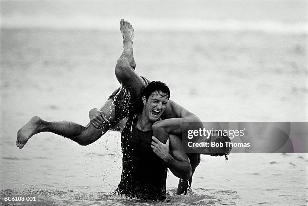 two young men playfully throwing each other about in sea (b&w) - black and white couple stock pictures, royalty-free photos & images