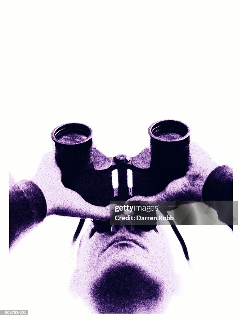 Man looking through binoculars, low angle view, close-up (toned B&W)