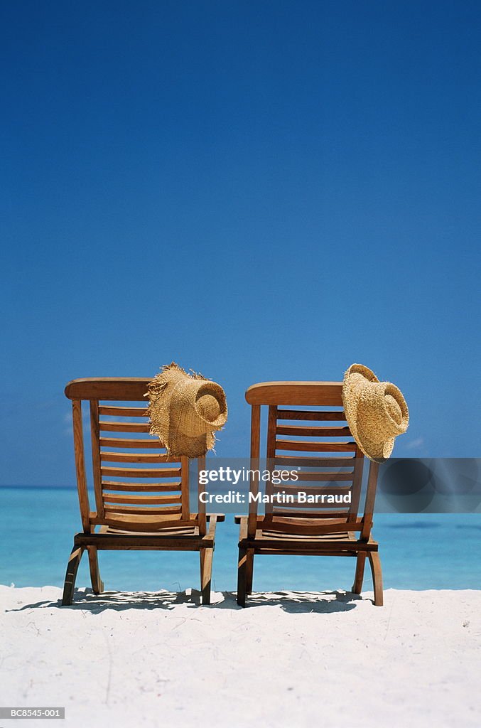 Two wooden deckchairs and straw hats on tropical beach, rear view