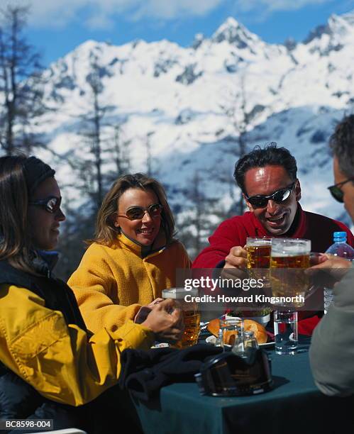four young people sitting around table drinking beer, outdoors - après ski stock-fotos und bilder