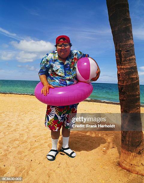 overweight man standing on beach, wearing inflatable ring, portrait - white socks stock-fotos und bilder