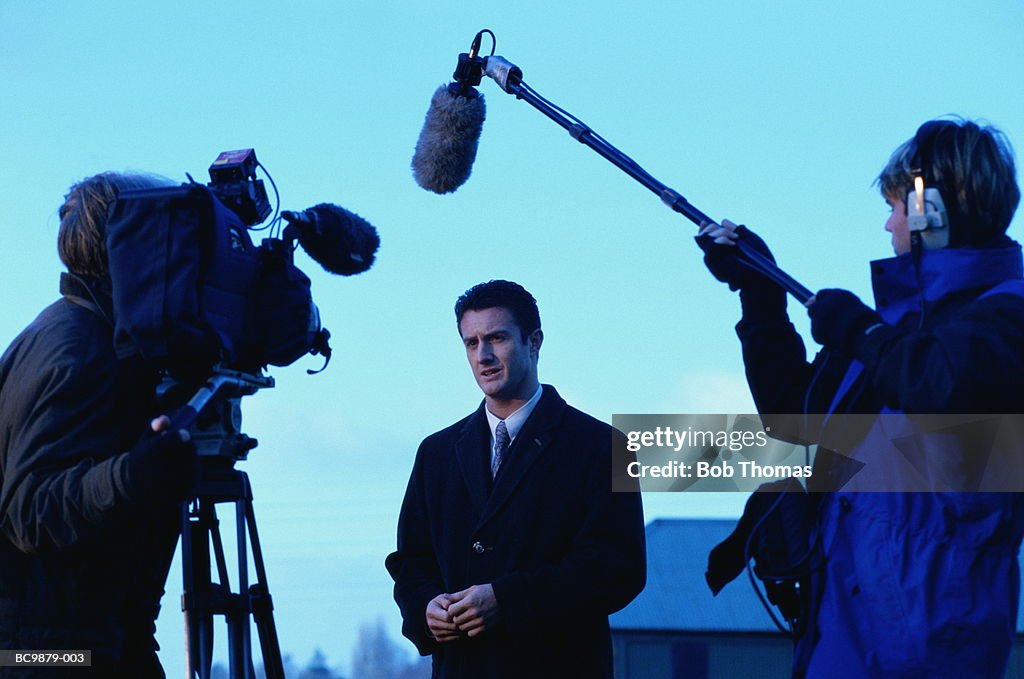 Television reporter talking to camera, outdoors at dusk