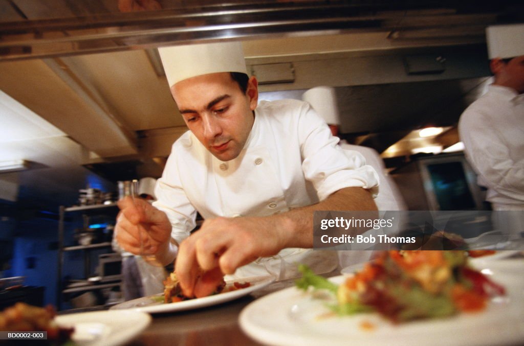 Male chef working in kitchen, arranging dish on plate, close-up