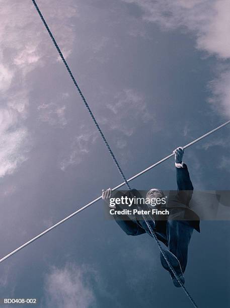 male executive walking on tightrope, upward view (toned b&w) - drahtseilakt stock-fotos und bilder