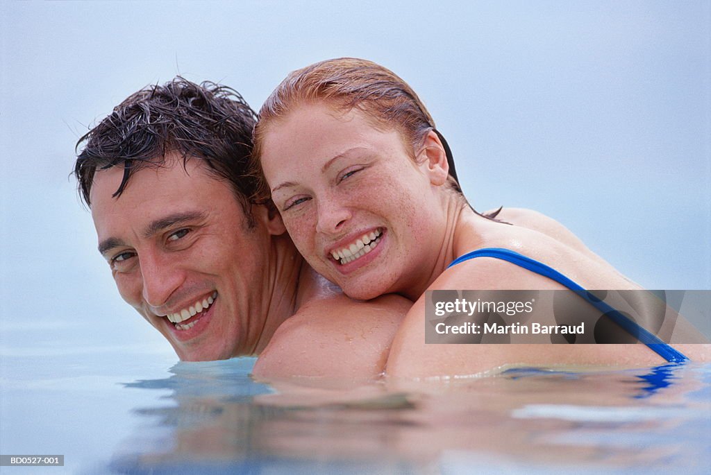 Couple embracing in sea, smiling, portrait