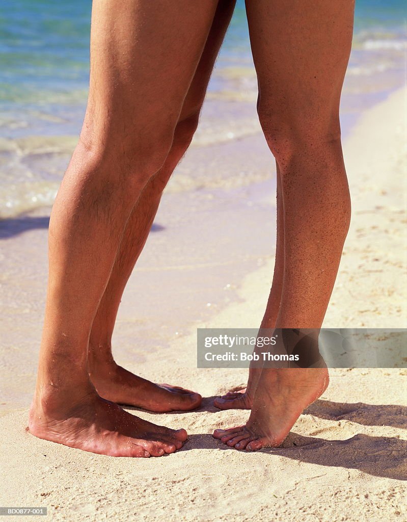 Couple kissing on beach, close-up of feet (low section)