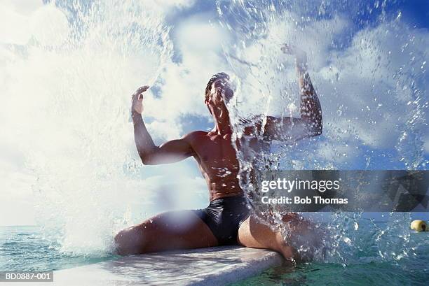 young man sitting on surfboard in sea, surrounded by water spray - surrounding ストックフォトと画像