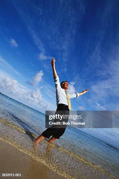 businessman paddling in sea, arms raised - rolled up trousers stock-fotos und bilder
