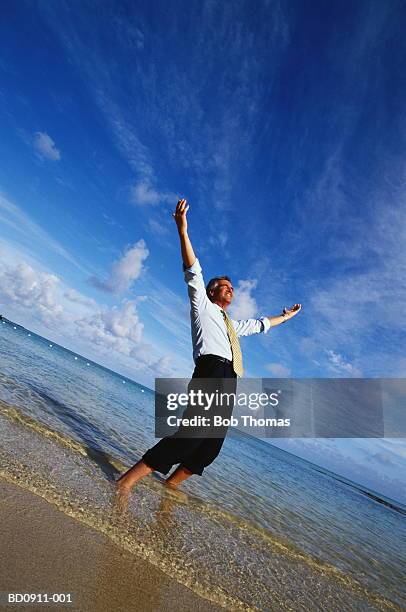 businessman paddling in sea, arms raised - ankle deep in water - fotografias e filmes do acervo